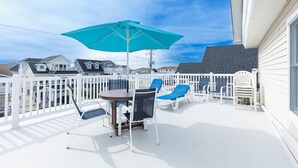 A covered outdoor deck with a table and chairs, a large umbrella, and a white fence.