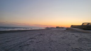 A beach with a clear sky at sunset, sandy terrain, and a structure on the right.