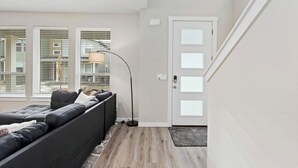 A modern living room with a sectional sofa, a floor lamp, and a door with frosted glass panels. - Meridian Family Home | King Bed | 4 TVs | Work From Home Setup | Freeway Access (Meridian)