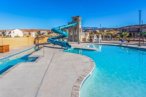 A swimming pool with a blue water slide, a lifeguard tower, and a clear view of the surrounding residential area.