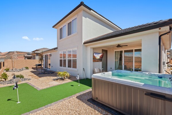 A modern two-story house with a hot tub, a patio with artificial grass, and a golf cart.