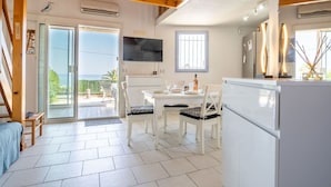 A modern kitchen with white cabinets, a dining area with white chairs, and a large sliding glass door leading to a balcony with a view of the sea. - Cosy apartment for 4 people with WIFI, A/C, TV, terrace and pets allowed (Fréjus)