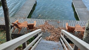 Una terraza de madera con sillas y barandilla, con vista a una masa de agua tranquila.