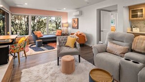 A modern living room with a grey sofa, a round ottoman, a wooden coffee table, and a large window with a view of trees. - Best Panoramic Views in Sedona, Hot Tub + Firepit! (Sedona)