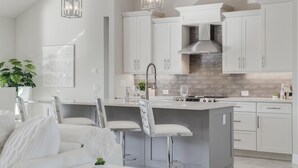 Une cuisine moderne avec des meubles blancs, un îlot central dot é de tabourets de bar et une hotte de cuisine en acier inoxydable.