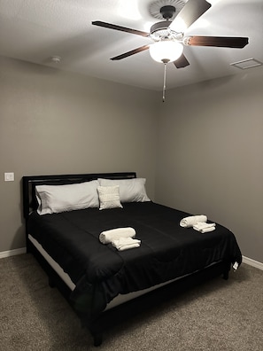A neatly made bed with black bedding and white pillows, a ceiling fan, and a smoke detector on the ceiling. - Zen Out. Relax. Vibe. Enjoy your Stay (El Paso)