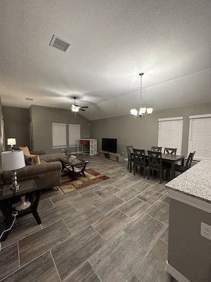 A spacious living room with a sofa, coffee table, and TV. There is a dining area with a table and chairs. The room has a ceiling fan and a chandelier. - Zen Out. Relax. Vibe. Enjoy your Stay (El Paso)