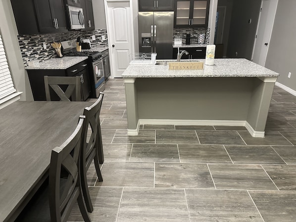 A modern kitchen with dark cabinetry, a granite countertop, and a herringbone-patterned backsplash. - Zen Out. Relax. Vibe. Enjoy your Stay (El Paso)