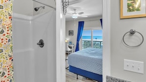 Ein Badezimmer mit Dusche, Deckenventilator und Blick auf einen Balkon mit einem Bett.
