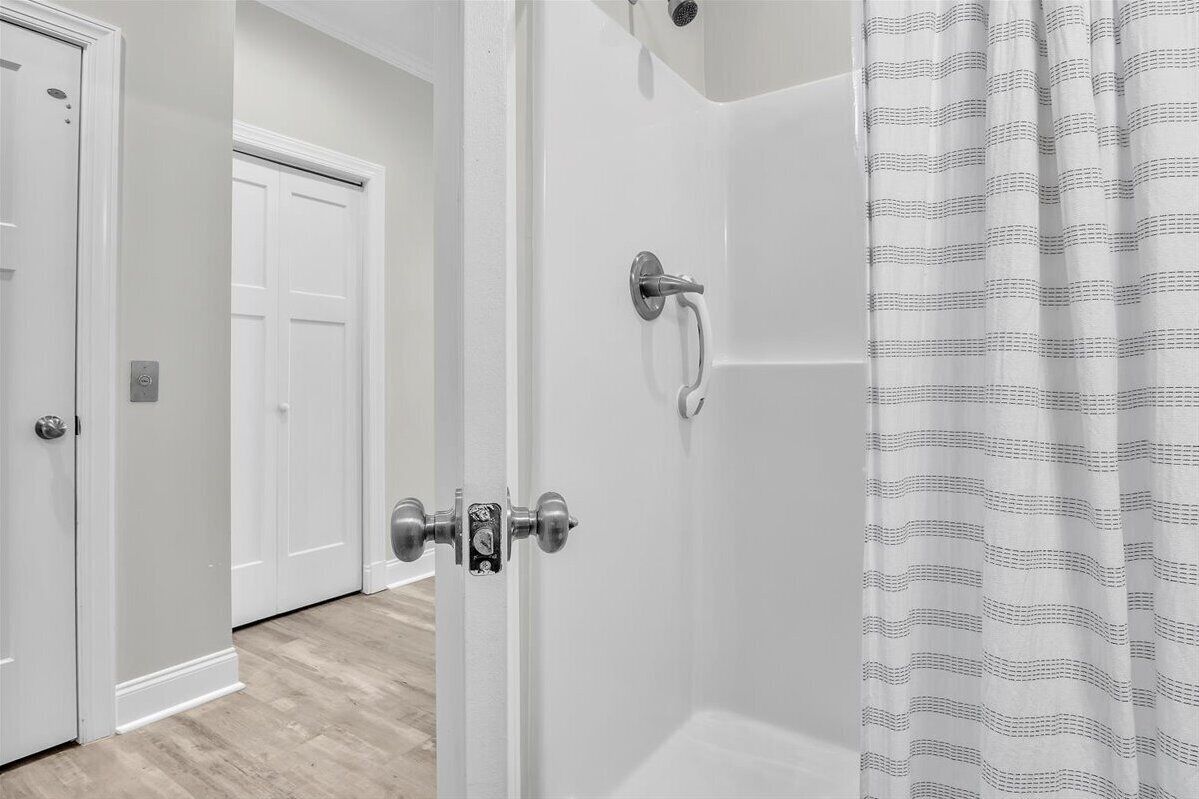Een badkamer met een douche, een witte deur en een douchegordijn met een patroon.