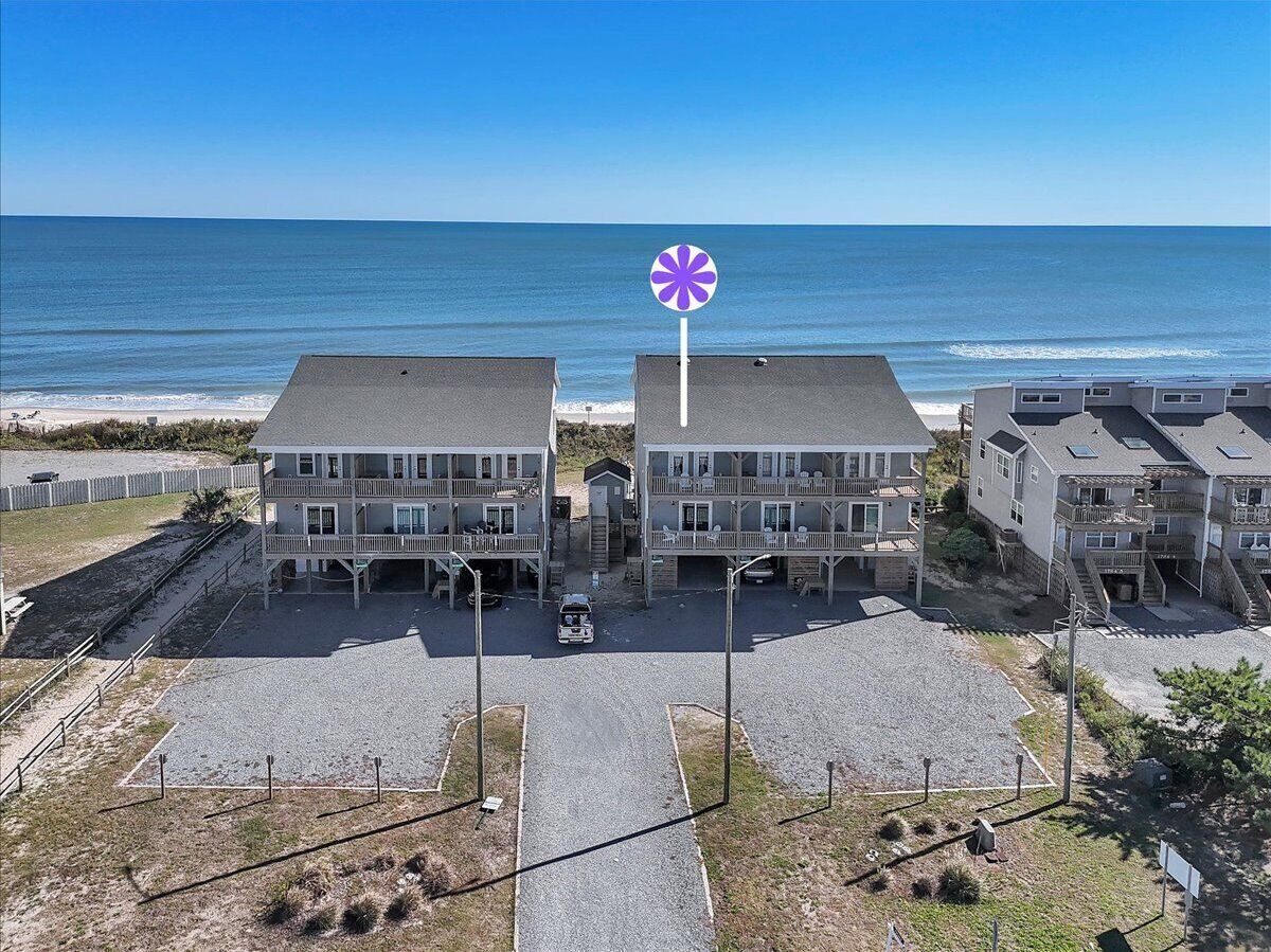 A beachfront hotel with a central parking area, multiple balconies, and a view of the ocean.