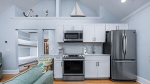 Una cocina compacta con armarios blancos, un refrigerador de acero inoxidable, un microondas y un horno.
