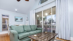 Una sala de estar con un sofá verde, una mesa de centro de madera y un amplio ventanal corredizo con cortinas.