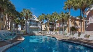 A swimming pool with lounge chairs and palm trees, surrounded by multi-story buildings with balconies.