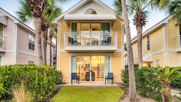 A two-story building with a balcony, surrounded by palm trees and a well-maintained lawn.