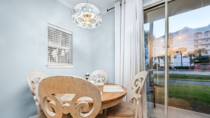 A dining area with a round table, wooden chairs, a stained glass chandelier, and a window with blinds.