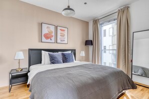 Ein modernes Schlafzimmer mit einem großen Bett, zwei Nachttischen, einer Stehlampe und einem Fenster mit Vorhängen.