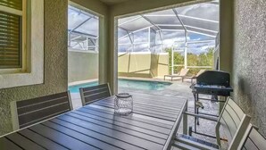 Eine überdachte Terrasse mit Pool, Gartenmöbeln und Grill.