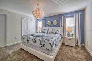 A bedroom with a floral bedspread, a hanging light fixture, a nightstand with a lamp, and two wall mirrors. - 8973CCD: Beautifully Decorated 4 Bedroom Townhome in ChampionsGate! (Davenport)