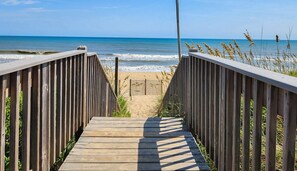 Ein hölzerner Steg führt zu einem Strand mit freiem Blick auf das Meer.