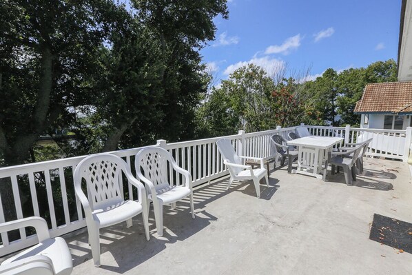 A covered outdoor patio with white plastic chairs and a table, surrounded by a white railing. - Sound Reflections - 4 BR Soundside home in Monteray Shores Corolla w/Private Pool (Corolla)