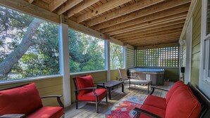 A covered porch with wooden beams, red cushioned chairs, a wooden table, and a colorful rug.