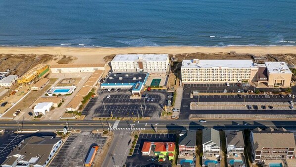 Vista aérea de un complejo hotelero frente al mar, con varias edificaciones, zonas de estacionamiento y una playa al fondo.