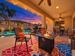 An outdoor patio with a pool, lounge chairs, a fire pit, and a ceiling fan.