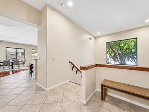 A modern interior with a staircase, a dining area, and a view of greenery outside.