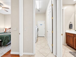 A hotel hallway with a bed, a washing machine, and a bathroom with a towel rack.