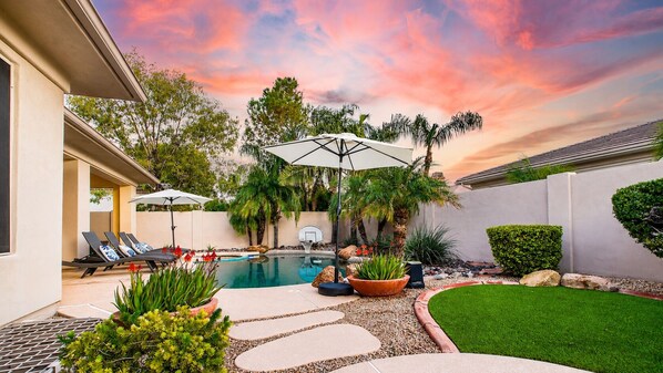 A backyard with a swimming pool, sun loungers, and potted plants.