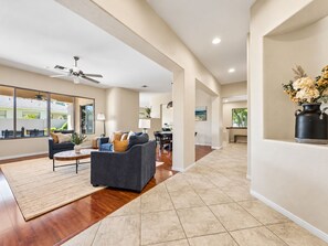 A spacious living area with a dark grey sofa, a wooden coffee table, and a large window offering a view of the outdoors.