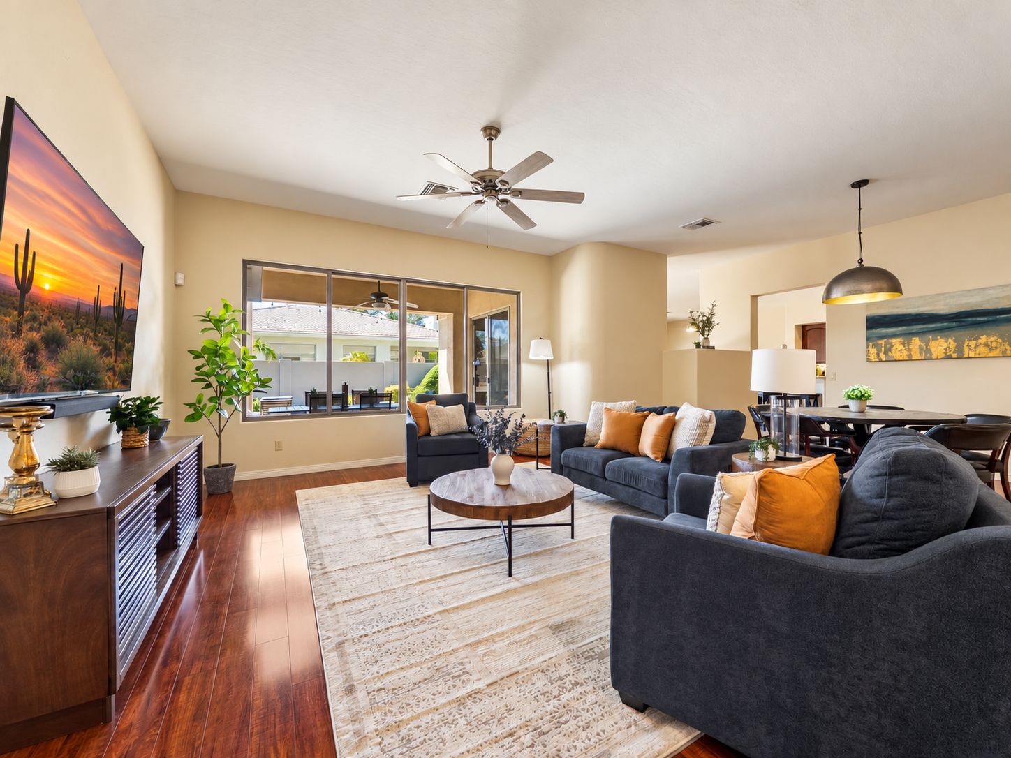 A spacious living room with a large window, a ceiling fan, and a dining area with a table and chairs.