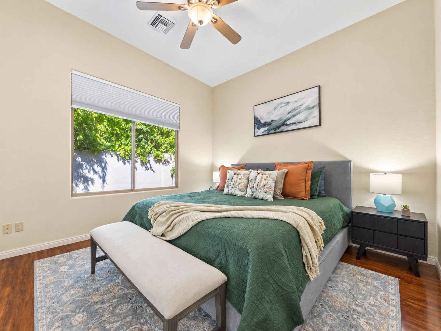 A bedroom with a bed, bench, nightstand, lamp, and a ceiling fan.