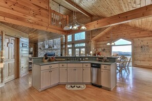 A spacious kitchen with a large island, wooden ceiling beams, and a view of the outdoors. - Carter`s Lake Overlook | Ellijay, Ga (Ellijay)