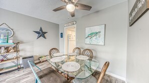 Comedor con mesa de vidrio, sillas de madera, ventilador de techo, decoración con estrella y un cuadro enmarcado de tortuga marina.