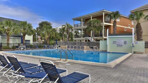 Una piscina con sillas de descanso, palmeras y un edificio con balcones.
