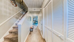A hallway with a wooden staircase, a bench, and a door with louvered shutters.