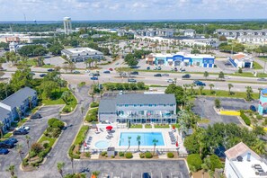 A hotel with a swimming pool, multiple parking lots, and a view of the surrounding area.