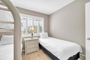 A bedroom with a bunk bed, a bedside table with a lamp, and a window with shutters. - Southbay by the Gulf 99 – Spacious Townhome with Private Beach Access (Destin)