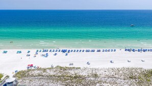 A beach with white sand, clear blue water, and numerous blue umbrellas. - Southbay by the Gulf 99 – Spacious Townhome with Private Beach Access (Destin)