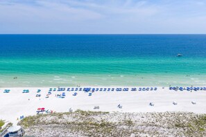 A beach with white sand, clear blue water, and numerous blue umbrellas. - Southbay by the Gulf 99 – Spacious Townhome with Private Beach Access (Destin)