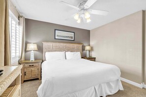 A hotel room with a bed, two bedside tables with lamps, a ceiling fan, and a framed picture on the wall.