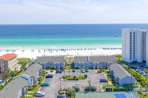 A beachfront hotel with a parking lot, a tennis court, and a view of the ocean.