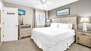 A bedroom with a large bed, a ceiling fan, a window with curtains, a bedside table with a lamp, and a door with a coat rack. - Southbay by the Gulf 99 – Spacious Townhome with Private Beach Access (Destin)