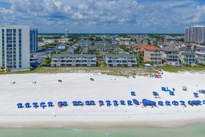Una playa con hileras de sombrillas azules y una fila de edificios frente al mar.