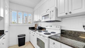 A kitchen with white cabinets, a microwave, a stove, and a trash bin. - Southbay by the Gulf 99 – Spacious Townhome with Private Beach Access (Destin)