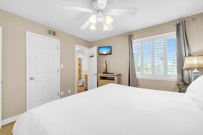 Une chambre d’hôtel avec un lit, un téléviseur fixé au mur, une fenêtre avec des rideaux et un ventilateur de plafond.