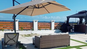 An outdoor patio with a large umbrella, wicker furniture, and a grill area. - Lux Sea View Camelot Village Discovery Bay (Discovery Bay)