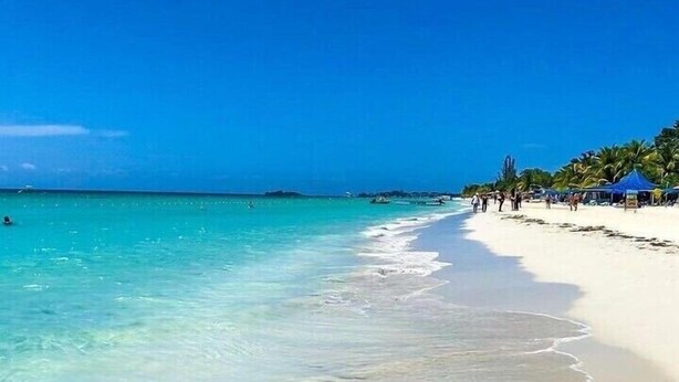 A beach with clear turquoise water, white sand, and a few people walking along the shore. - Lux Sea View Camelot Village Discovery Bay (Discovery Bay)